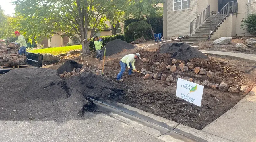 Workers from Rogers Landscape constructing a residential landscape, featuring piles of soil and rocks, with a sign promoting free estimates.