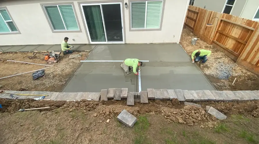 Workers pouring and leveling concrete for a patio installation, showcasing professional landscape construction services by Rogers Landscape.