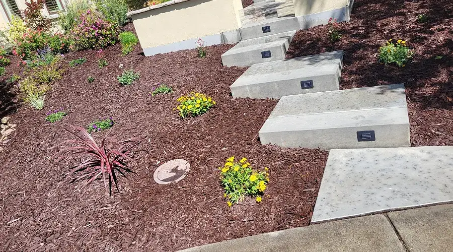 Concrete steps leading through landscaped garden with colorful flowers and mulch, showcasing hardscaping design by Rogers Landscape.