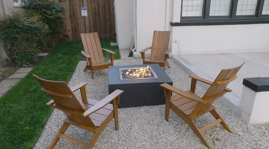 Fire pit surrounded by four wooden Adirondack chairs on a gravel patio, enhancing outdoor living space with warmth and comfort.