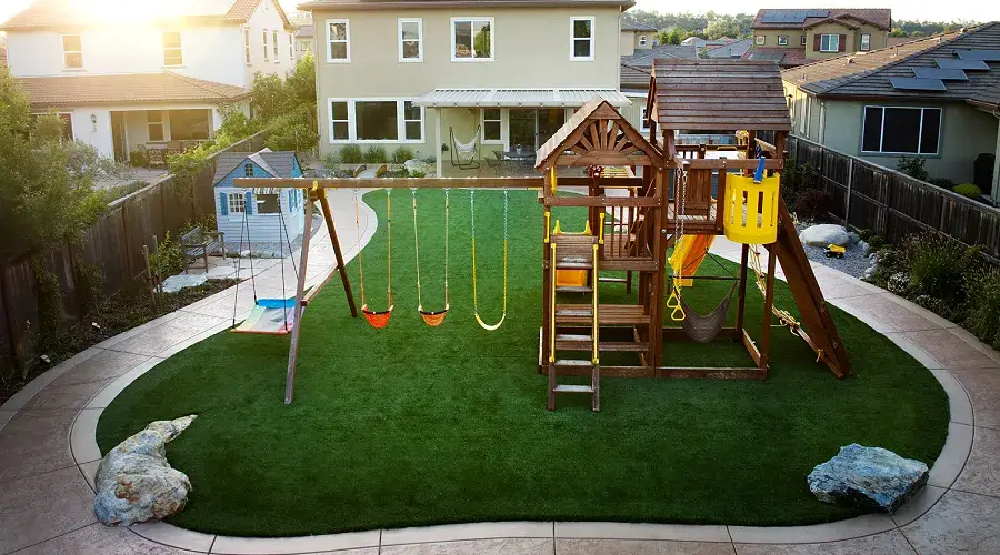 Backyard playground with wooden playset, swings, and artificial grass lawn, showcasing a sustainable, low-maintenance outdoor space ideal for family enjoyment.