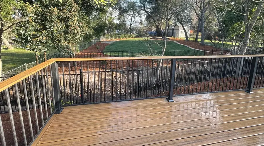 Deck view featuring a composite railing overlooking a landscaped yard with fencing and trees, highlighting outdoor living space design by Rogers Landscape.