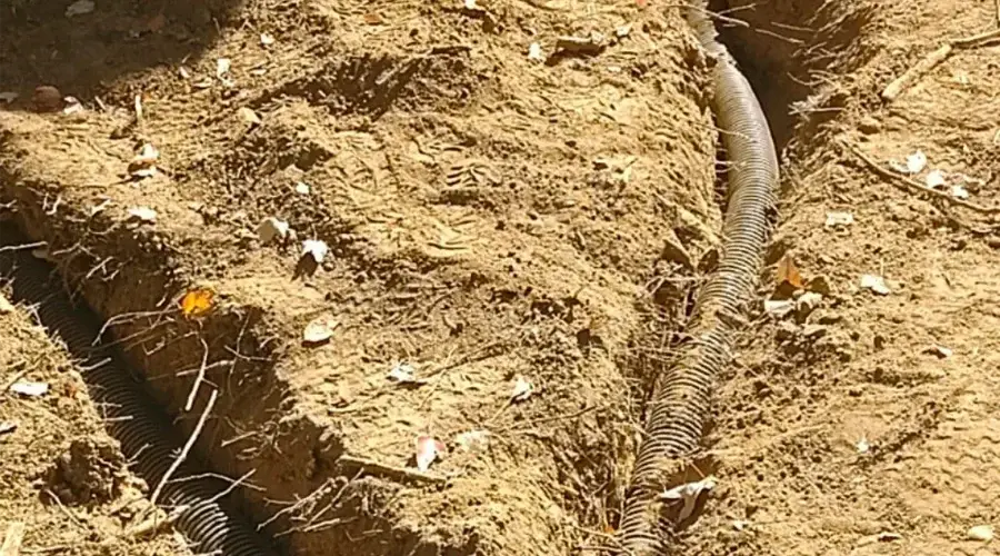 Drainage installation featuring perforated pipe laid in a trench, surrounded by loose soil and scattered leaves, emphasizing efficient water management for landscape protection.