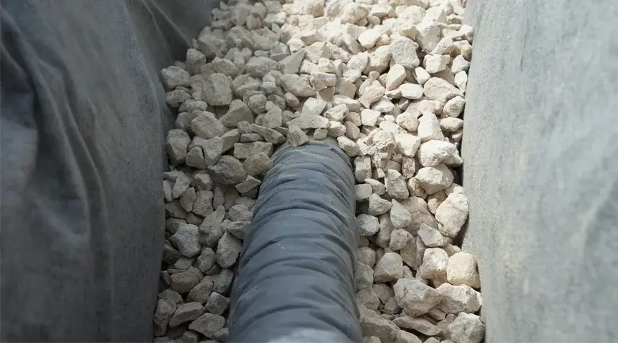 Drainage system installation featuring a perforated pipe surrounded by gravel, illustrating effective water management solutions for landscaping.