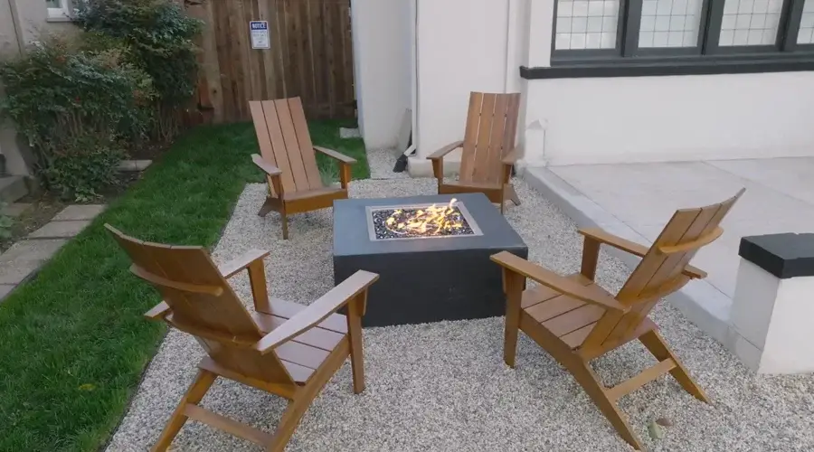Fire pit surrounded by wooden chairs on gravel patio, enhancing outdoor living space with a modern design.