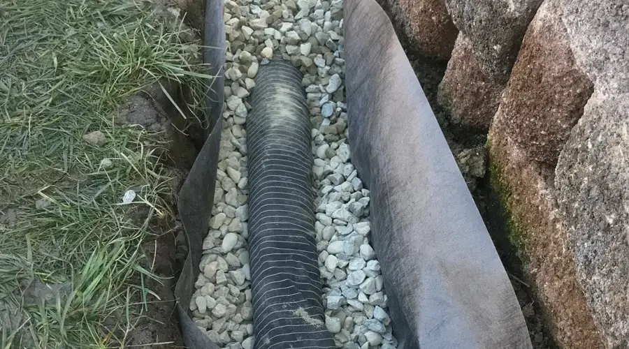 French drain installation with gravel and drainage pipe, designed for effective water management and erosion control in landscaping.