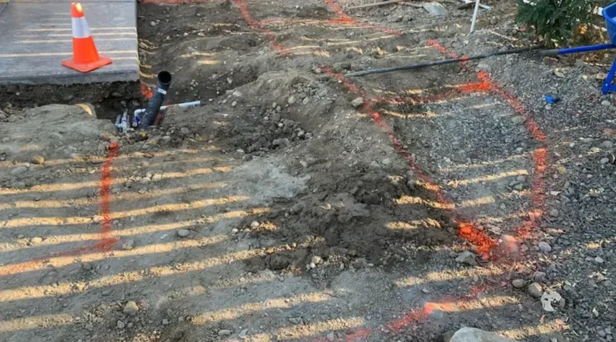 Excavated area for irrigation system installation with marked lines and a traffic cone, showcasing preparation for efficient water distribution in landscaping.