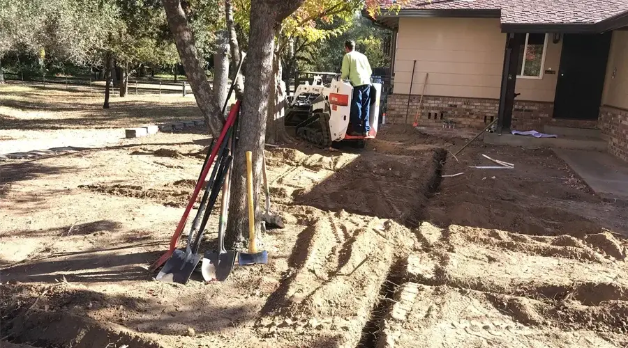 Irrigation system installation in progress, featuring a worker operating machinery on a prepared landscape area, surrounded by tools and equipment, highlighting the commitment to efficient drainage and irrigation solutions by Rogers Landscape.