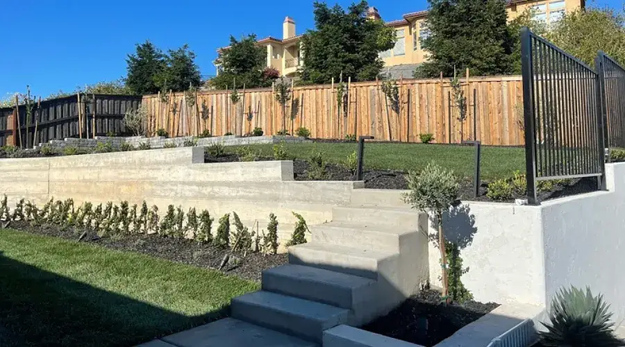Landscaped outdoor space featuring tiered green lawn, mulched flower beds, and decorative fencing, illustrating cohesive design and sustainable choices by Rogers Landscape in California.