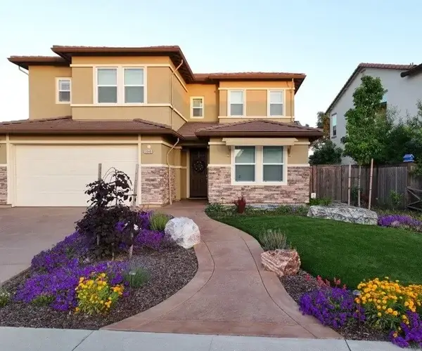 Residential landscape design featuring a two-story home in Folsom, CA, with a decorative pathway, vibrant flower beds, and well-maintained greenery, showcasing the potential for beautiful outdoor living spaces.