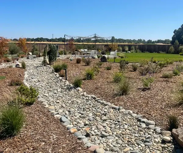 Residential landscaping in Orangevale, CA, featuring a stone pathway, lush plants, and outdoor seating area, showcasing functional and aesthetic outdoor living spaces.