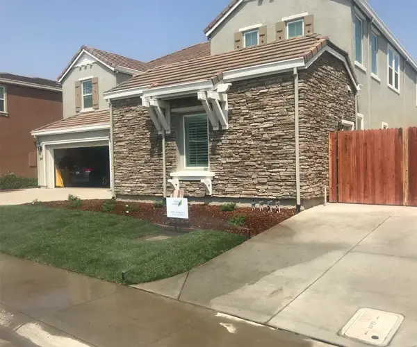 Residential landscaping project showcasing a modern home in Rocklin, CA, featuring stone exterior, manicured lawn, and decorative landscaping elements.