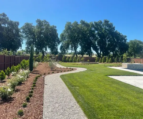 Landscaped backyard featuring a winding gravel pathway, lush green lawn, and decorative shrubs, showcasing quality landscaping services by Rogers Landscape in Roseville, CA.