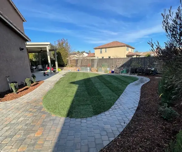 Residential landscaping featuring a curved stone patio, lush green lawn, and well-maintained garden area in Sacramento, CA, showcasing high-end outdoor living design by Rogers Landscape.