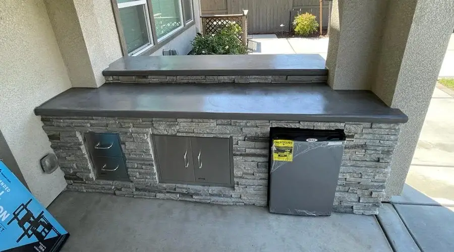Outdoor bar counter with stone base, sleek countertop, and built-in refrigerator, showcasing quality craftsmanship and durability for outdoor dining spaces.