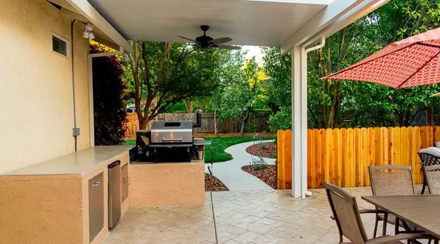 Luxury outdoor kitchen with grill, counter space, and dining area, surrounded by lush greenery and a winding pathway, showcasing Rogers Landscape's custom outdoor living design.