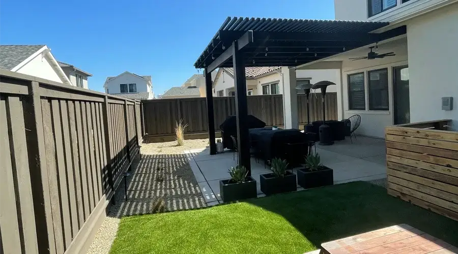 Modern outdoor living space with a shaded pergola, comfortable seating area, decorative planters, and artificial grass, designed for relaxation and entertainment.