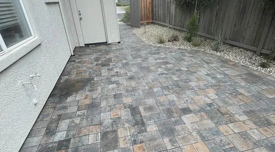 Paver walkway featuring a blend of gray and brown stones, leading to a door, surrounded by low-maintenance landscaping and a wooden fence, illustrating quality outdoor design by Rogers Landscape.