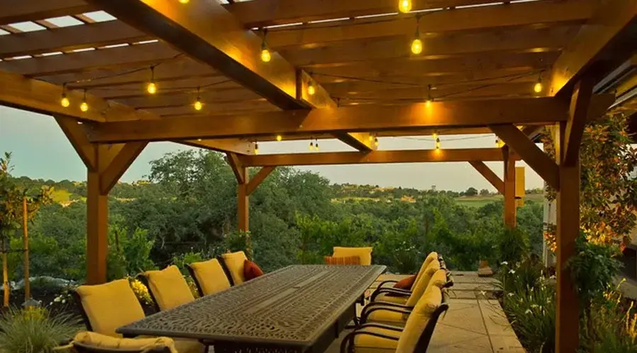 Custom wooden pergola with string lights, outdoor dining table, and lush greenery in Loomis, CA, enhancing outdoor living space.