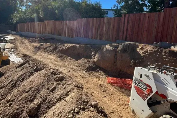 Excavated landscape area with machinery, gravel, and wooden fence, illustrating drainage installation and site preparation for landscaping renovations in Rocklin, CA.
