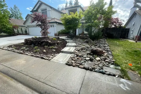 Residential landscape featuring a curved stone pathway, decorative rock beds, and drought-tolerant plants, enhancing curb appeal in Northern California.