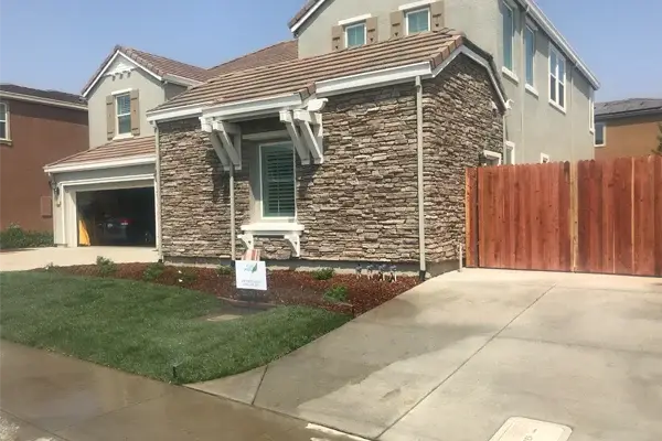 Residential landscaping featuring a stone-accented home, manicured lawn, and wooden fence, showcasing Rogers Landscape's design and installation services in Granite Bay, CA.