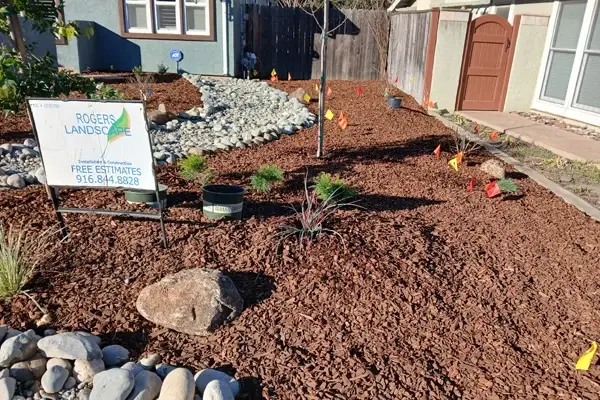 Residential landscaping by Rogers Landscape in Granite Bay, CA, featuring decorative rock, mulch, and newly planted greenery, with a sign promoting free estimates.