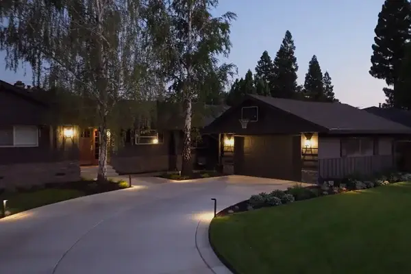 Driveway illuminated by low-voltage landscape lighting, enhancing the exterior of a home with a basketball hoop, surrounded by greenery and trees, showcasing Rogers Landscape's outdoor lighting services in Granite Bay, CA.