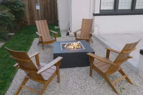 Custom outdoor living area with four wooden Adirondack chairs surrounding a fire pit on gravel, enhancing functionality and aesthetic appeal for entertaining.