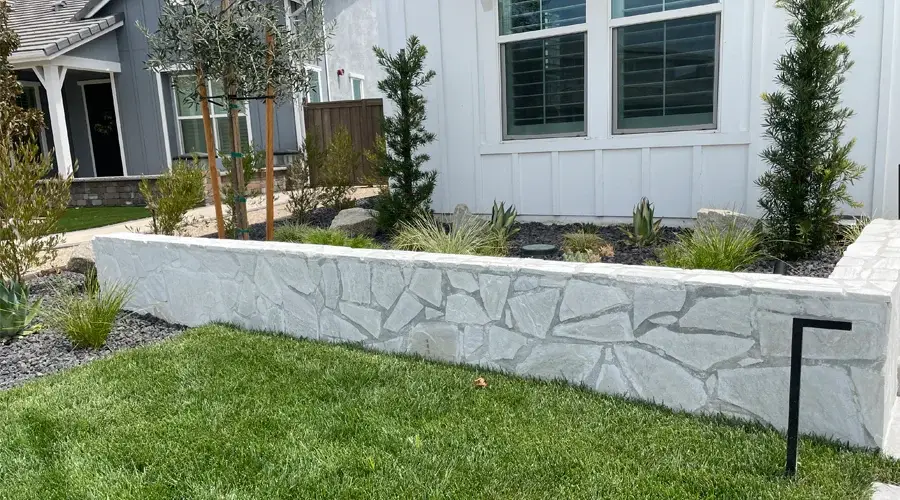 White stone seat wall integrated into a landscaped garden with green grass, ornamental plants, and a modern home exterior.