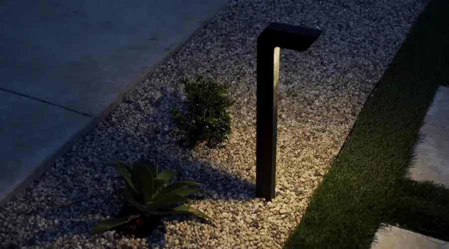 Modern outdoor uplight illuminating a landscaped area with gravel, featuring plants and grass, enhancing the backyard's atmosphere.
