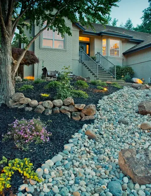 Residential landscape design featuring a well-maintained front yard with decorative rock pathways, flowering plants, and a modern home entrance, illustrating Rogers Landscape's commitment to quality outdoor spaces.