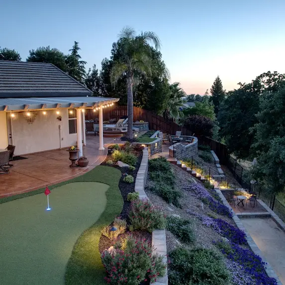 Landscape construction by Rogers Landscape in Loomis, CA, featuring a well-designed backyard with a putting green, lush plants, and outdoor seating under ambient lighting.