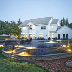 Luxury residential landscape design featuring a modern home with illuminated outdoor spaces, terraced gardens, and a pool area, showcasing Rogers Landscaping's expertise in high-end landscape transformations.
