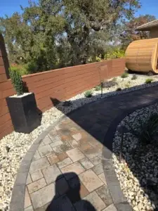 Curved stone pathway in a landscaped garden with planters and a wooden barrel.