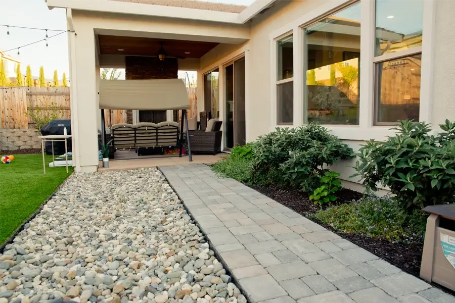 Concrete patio pathway leading to a cozy outdoor seating area, surrounded by lush greenery and