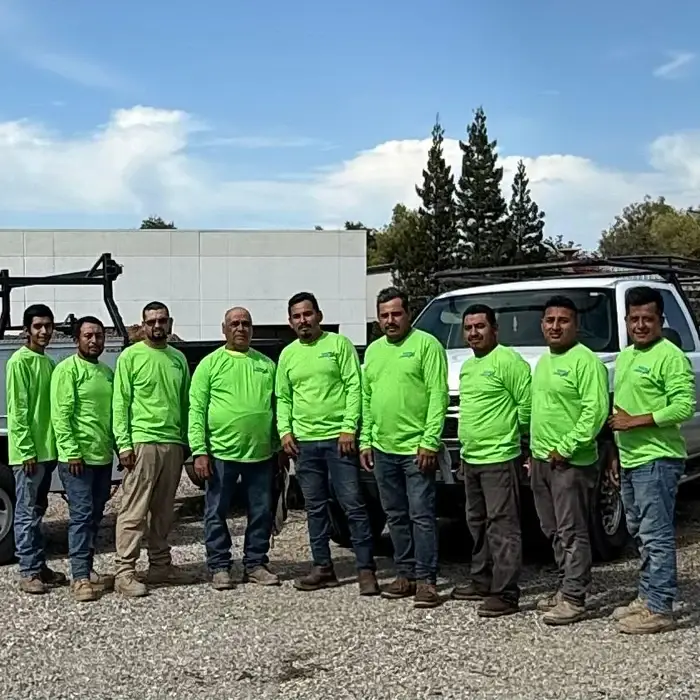 Rogers Landscape crew in bright green shirts standing together in front of company work trucks in Loomis, CA